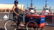 Photo of smiling woman on a bike with a book box on a pier