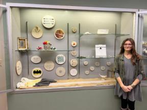 The artist standing with her craft items in a display case.