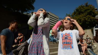 Photo of two girls watching eclipse through solar glasses with awed expressions