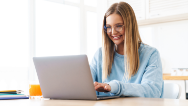 Photo of a woman researching at home, smiling sweetly at her laptop.