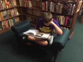 Photo of teen wearing KV shirt reading on cushioned chair in book shop.