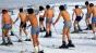 Photo of skiers on slope, all wearing shorts with no shirts or belly shirts.